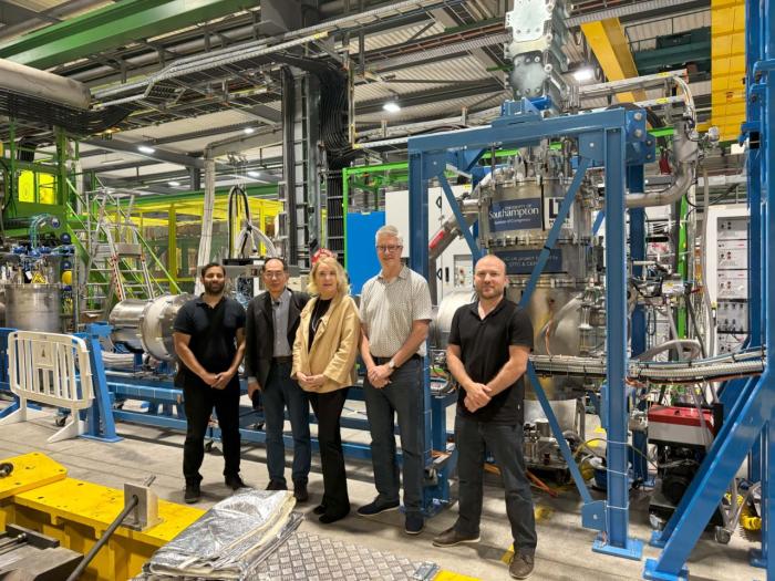 five people smiling in front of silver and blue equipment